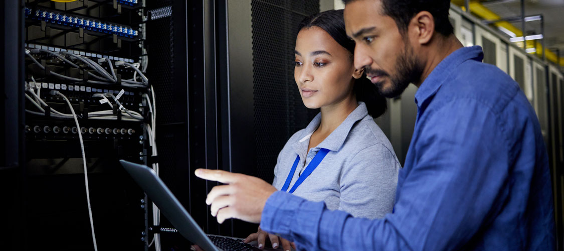 People looking at laptop in server room